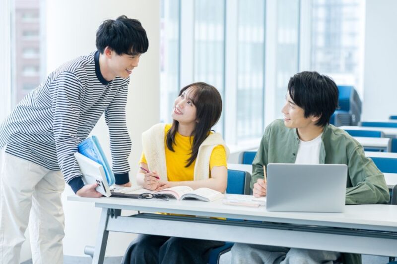 大学でにこやかに話をしている男女の学生３名