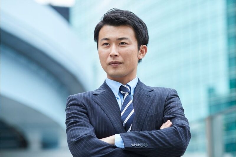 会社のビルの前で腕を組むスーツの男性