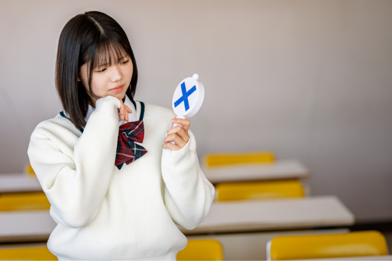 バツの札を持つ女子高生